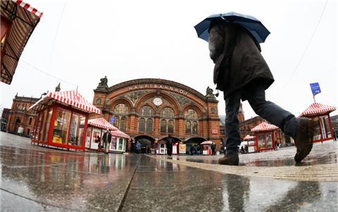 31.03.2018, Bremen: Ein Mann geht mit einem Regenschirm in Richtung Bremer Hauptbahnhof. 