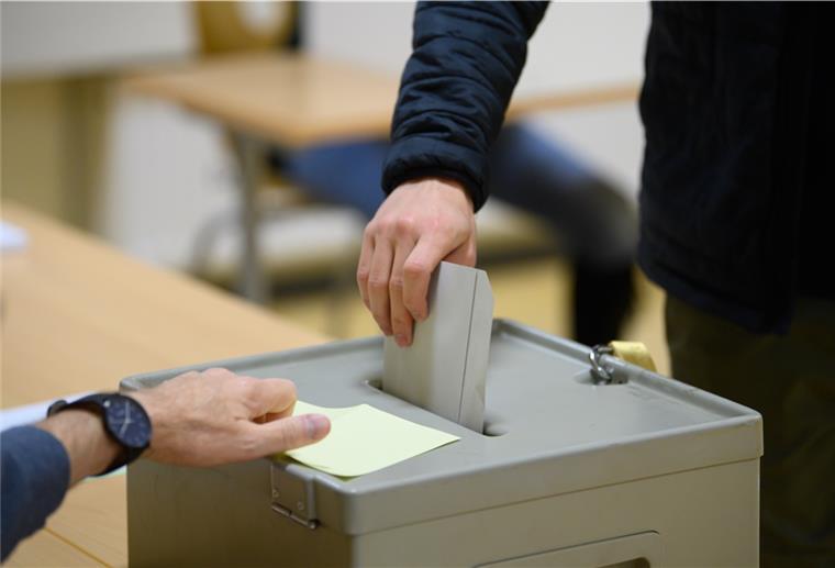 Person steckt Wahlzettel in Urne.