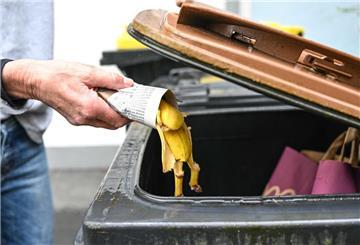 Eine Frau wirft in Zeitungspapier gewickelte Bananenschalen in eine Mülltonne für den Biomüll.