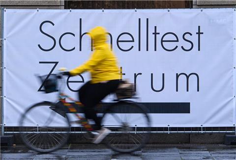 Eine Fahrradfahrerin fährt an einem Banner mit der Aufschrift "Schnelltest Zentrum" vorbei. 