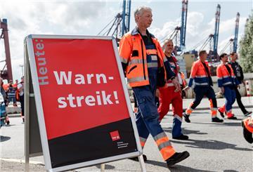 Hafenarbeiter gehen an einem Schild mit der Aufschrift "Warnstreik!" vorbei zu einer Streikversammlung. 