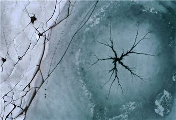 Ein sternförmiger Riss ist auf der Eisfläche des Forggensees neben am Ufer liegenden gebrochenen Eisplatten zu sehen (Luftaufnahme mit einer Drohne).