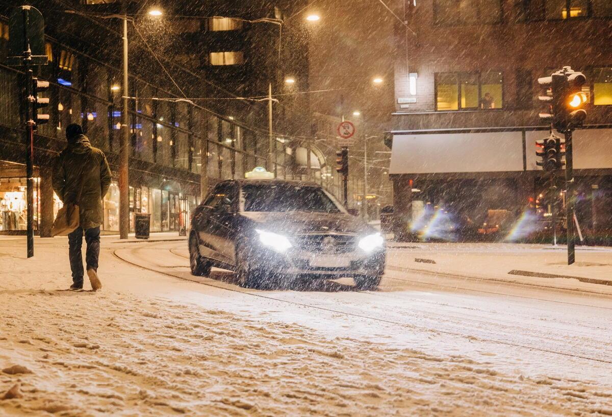 Bei Schneefall fährt ein Auto durch die Straßen. Es ist dunkel.