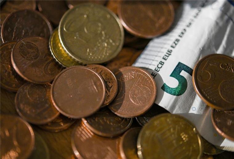 Millionen Menschen sind betroffen! Ab diesem Einkommen gilt man in Deutschland als arm Geldmünzen und ein 5 Euro-Schein liegen in einer Schale.