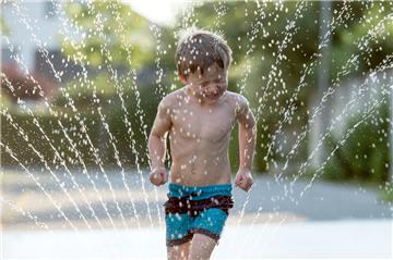 Abkühlung während der Hitzewelle: Kinder genießen gerne die Wasserstrahlen eines Rasensprengers, der den Rasen grün halten soll. Dabei wird allerdings auch viel Wasser verbraucht.