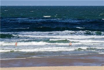 Strandbesuchende stehen bei sommerlichem Wetter in der Nordsee-Brandung am Strand in Westerland.