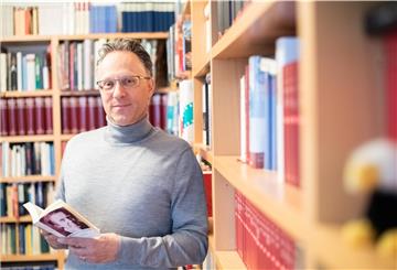 Sebastian Loskant mit Gedichtband von Robert Gernhardt vor Bücherwand.