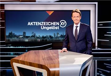 «Aktenzeichen XY... Ungelöst»-Moderator Rudi Cerne steht im Studio und lächelt in die Kamera.