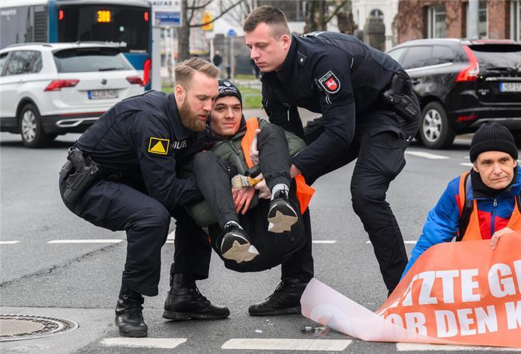 Aktivisten der Umweltgruppe Letzte Generation haben sich auf dem Gorch-Fock-Wall am Stephansplatz in Hamburg festgeklebt und wollen damit auf die Einhaltung der Klimaziele aufmerksam machen. Polizisten sprechen mit den Aktivisten - hier mit Fabian B. aus Zeven.