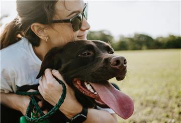 Eine Frau mit Sonnenbrille umarmt einen braunen Hund.