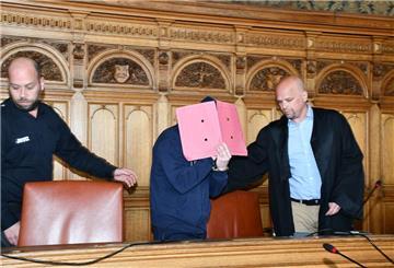 Angeklagter wird mit Mappe vorm Gesicht zum Platz geführt