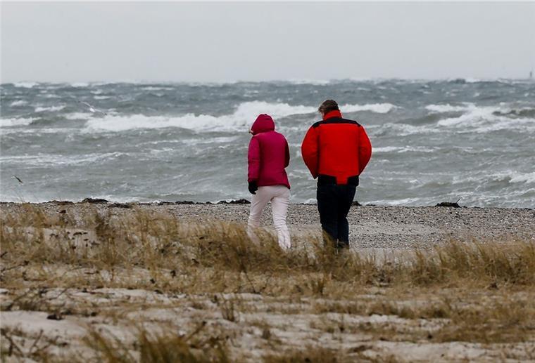 Zwei Personen gehen bei stürmischen Wetter am Strand spazieren.