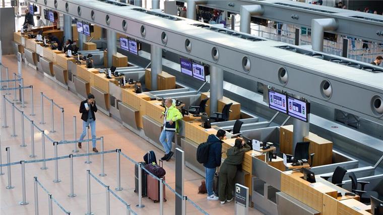 Am Flughafen in der Stadt Hamburg stehen einige Leute mit ihrem Gepäck. Wegen eines Warnstreiks gingen dort am Sonntag nur wenige Flugzeuge in die Luft.