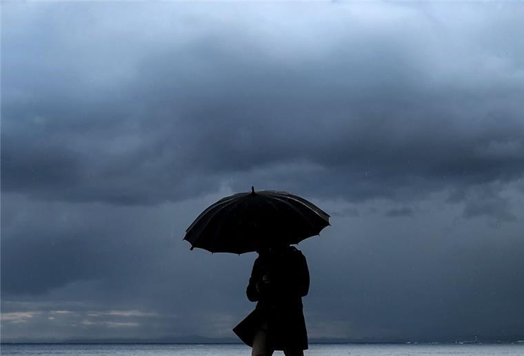 Ein Mann hält einen Regenschirm, während er am Meer entlang spazieren geht.