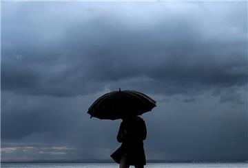 Ein Mann hält einen Regenschirm, während er am Meer entlang spazieren geht.