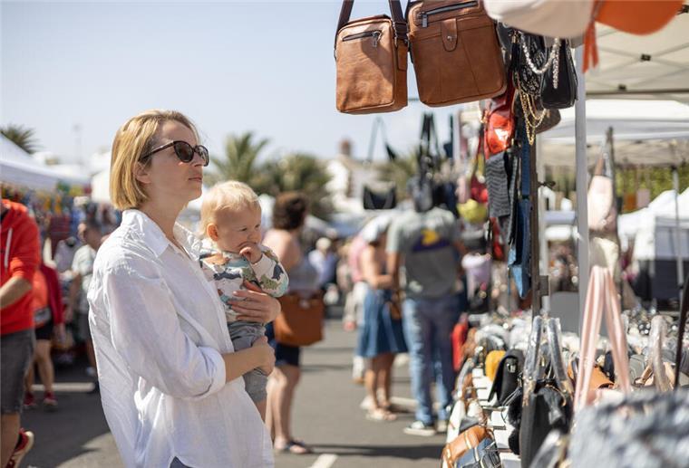 Eine Frau hält ein Baby auf dem Arm und schaut sich auf einem Flohmarkt um.