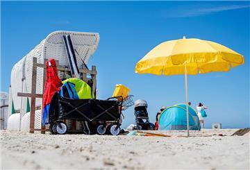 Ein Sonnenschirm steht bei sonnigem Wetter neben einem Strandkorb am Strand von Norddeich.