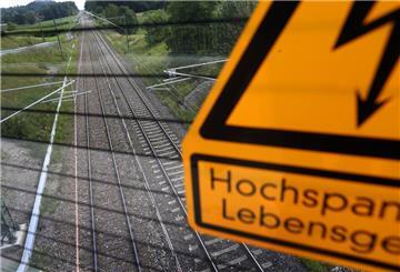 Auf einer Brücke über der mit neuen Masten und Stromleitungen versehenen Bahnstrecke München-Lindau warnt ein Schild vor Hochspannung.