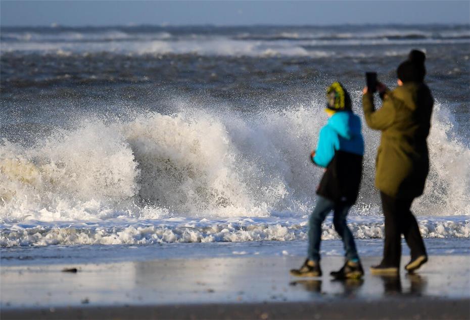 Eine Frau steht mit einem Kind am Strand vor den tosenden Wellen der Nordsee