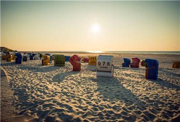 Mehrere Strandkörbe stehen am Strand und die Sonne geht unter.