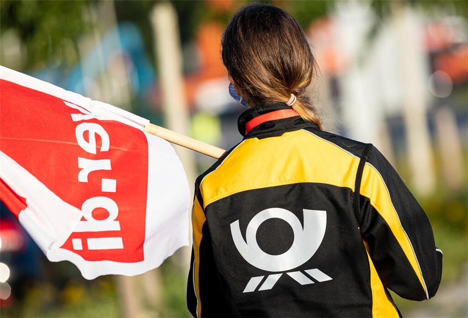 Eine Beschäftigte der Deutschen Post steht mit einer Fahne der Gewerkschaft Verdi vor der Deutsche-Post-DHL-Niederlassung