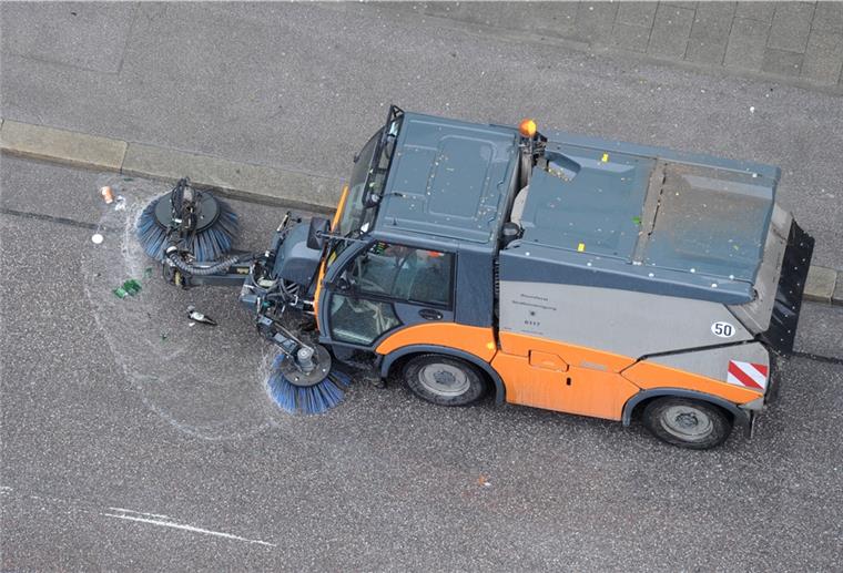Ein Kehrfahrzeug der Straßenreinigung fährt auf einer Straße während die Bürsten des Fahrzeugs im Einsatz sind.