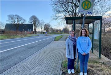 Mutter und Tochter stehen vor einem Buswartehäuschen.