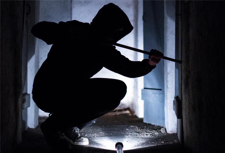 Ein fiktiver Einbrecher hebelt mit einem Brecheisen eine Tür im Keller eines Wohnhauses auf
