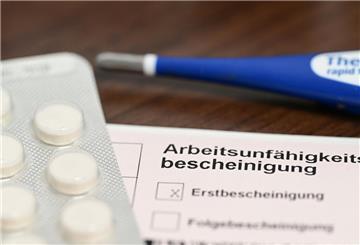 Ein Fieberthermometer, Medikamente und eine ärztliche Arbeitsunfähigkeitsbescheinigung (Krankmeldung) liegen auf einem Nachttisch (gestellte Szene).