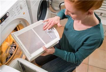eine Frau leert das Flusensieb eines Wäschtrockners