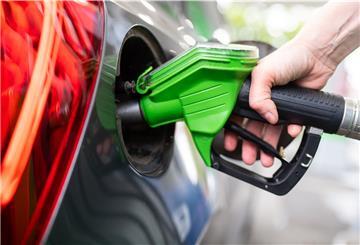 Eine Frau hält an einer Tankstelle an einer Zapfsäule eine Zapfpistole in der Hand und betankt ein Auto.
