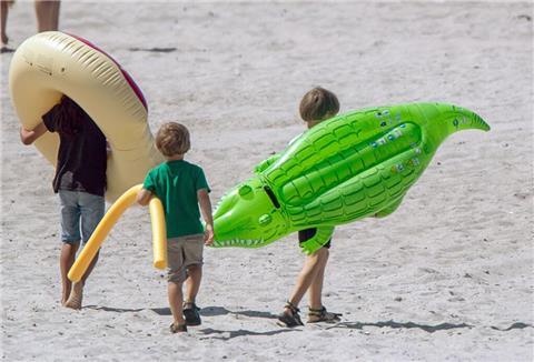 Kinder tragen ihre Schwimmhilfen zum Strand.