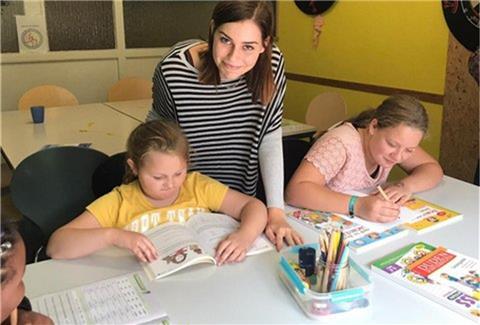 Eine junge Frau hilft zwei Mädchen beim Malen und Lesen.
