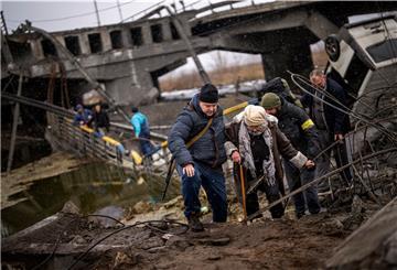 Örtliche Milizionäre helfen einer alten Frau über eine von Artillerie zerstörte Brücke am Stadtrand von Kiew. 