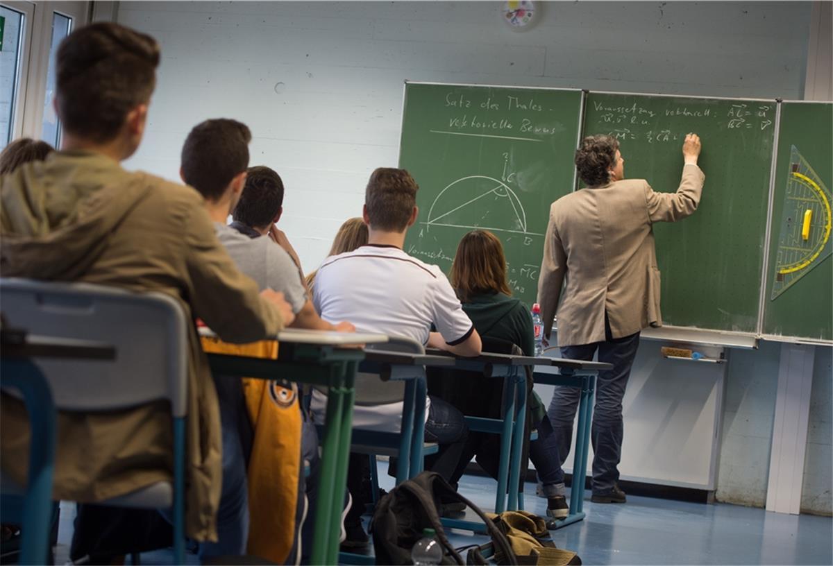 Ein Lehrer schreibt während des Matheunterrichts einer Abiturklasse an die Tafel. 