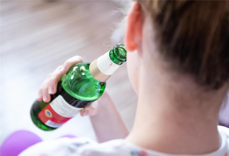  Ein Mädchen hält in ihrem Zimmer eine Flasche Bier.