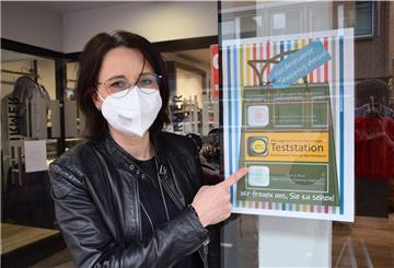 Auch Mode Irmer an der Bahnhofstraße in Nordenham ist von der Testpflicht betroffen. Das Foto zeigt Viola Irmer neben einem entsprechenden Plakat am Eingang.