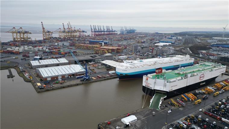 Auf dem Bild ist das Autoterminal in Bremerhaven zu sehen, im Hintergrund stehen Kräne des Containerterminals.