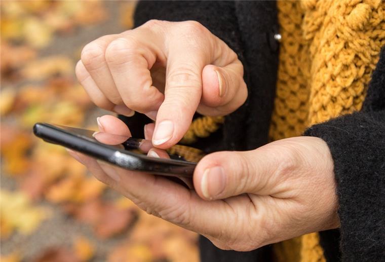 Frauenhände halten ein Handy und tippen auf den Bildschirm.