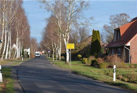 Ein Kleintransporter fährt auf einer Dorfstraße an Wohnhäusern vorbei
