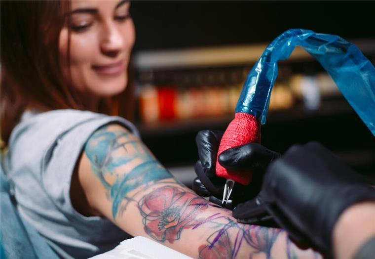 Bremerhaven rockt, Landkreis Cuxhaven lockt:Das ist am Wochenende los Eine Frau lässt sich tätowieren und lächelt dabei. In Bremerhaven findet am 15. und 16. März eine Tattoo-Messe statt, die sich an Frauen richtet.