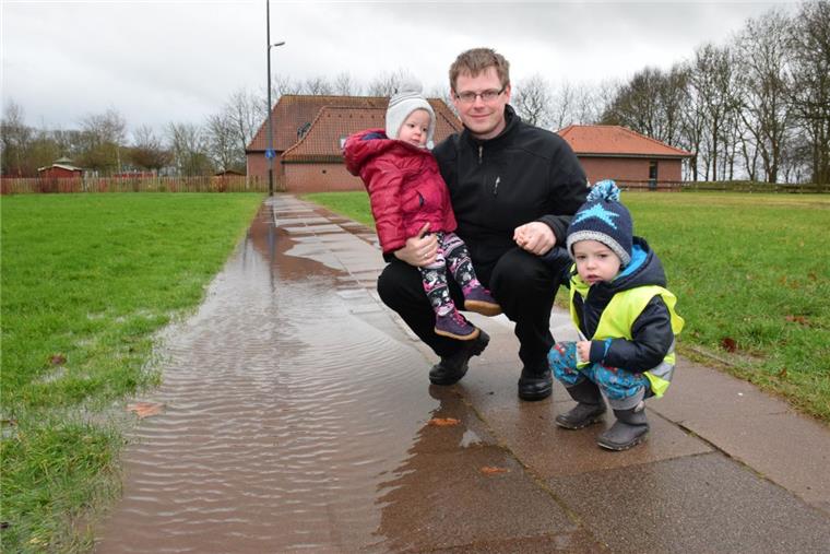 Weg zur Abbehauser Kita steht ständig unter Wasser Auf diesem Weg, der zum Abbehauser Kindergarten führt, stand gestern Morgen auf voller Breite das Wasser. Der Bauhof musste anrücken und das Wasser abpumpen. Jan Garbe – hier mit seinen beiden Kindern Lara und Lukas – fordert die Stadt auf, schnell tätig zu werden.