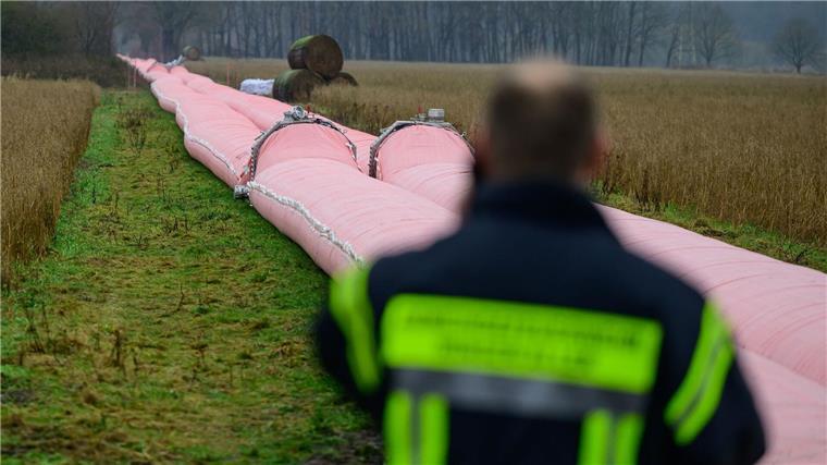 Auf einem Feld liegt ein Teil von einem mobilen Deich, welcher mit Wasser befüllt ist.