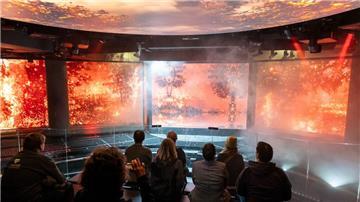 Auf einer sich bewegenden Plattform verfolgen Besucher Aufnahmen eines Waldbrandes.