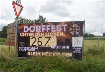 Ein Plakat steht neben einem Verkehrsschild in der Wiese.