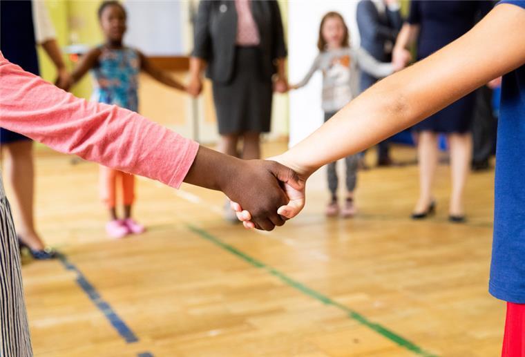 Hand in Hand tanzen Kinder und Erzieherinnen bei einem Bewegungsspiel in der Turnhalle einer Kita