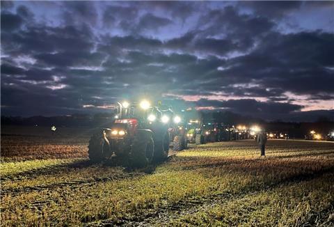 Beleuchtete Traktoren fahren zur Abendzeit auf eine Weide