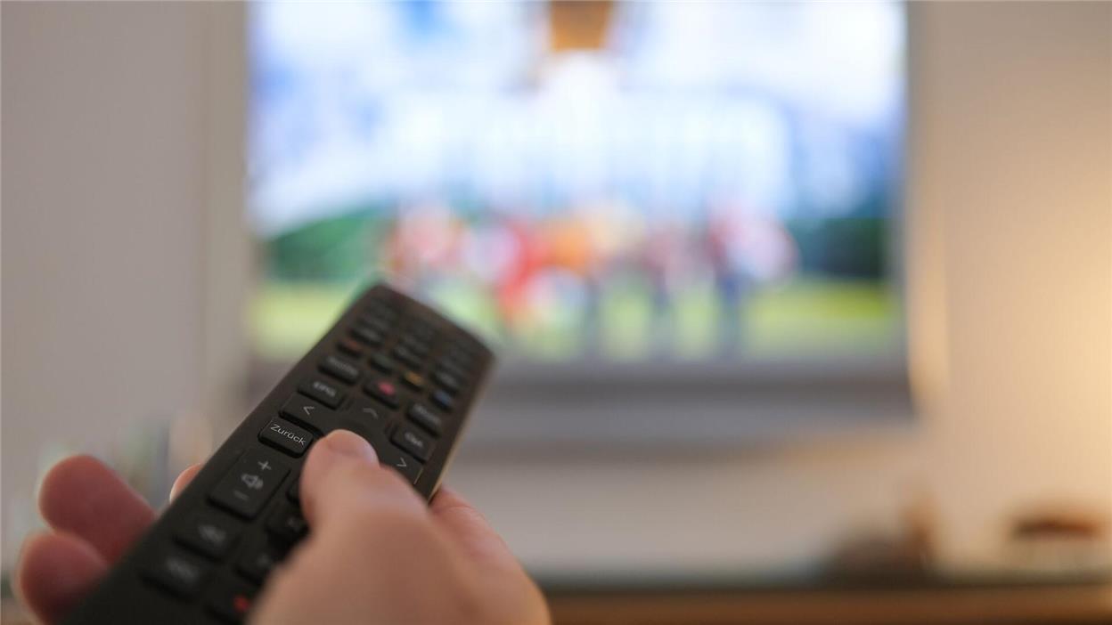 Eine Hand bedient eine Fernbedienung für ein TV-Gerät.