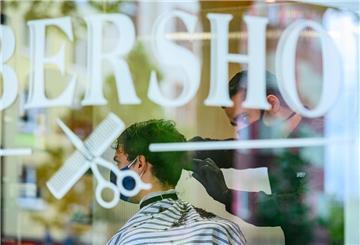 Auf einem Fenster klebt die Aufschirft Barbershop. Im Hintergrund werden einem Kunden die Haare geschnitten.