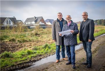 Bauunternehmer Anatoli Delgas (links) von EG Massivhausbau, Baustadtrat Bernd Schomaker (Mitte) und Finanzierungsberater Andre Wittmann stehen vor dem zu erschließenden Bauland am Plätternweg.